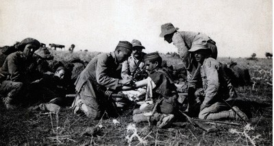 España. Campaña del Rif de 1921. Sanitarios españoles curando un soldado herido bajo el fuego enemigo en Irgueman. Tarjeta postal.