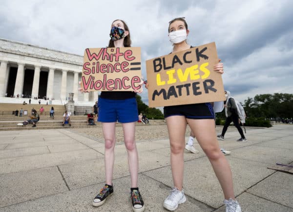 Women with signs reading ''White silence = violence'' and ''Black Live Matter''