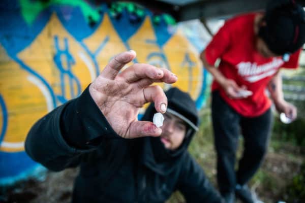 An addict sits on the street and shows his recently acquired drugs