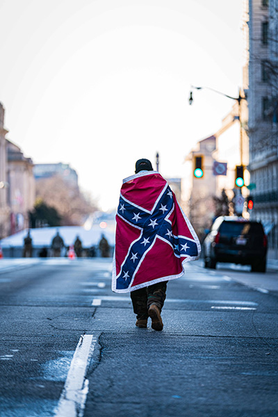 A man wearing a confederate flag walks down a Washington D.C. street during the 2021 Inauguration. (Credit Image: © Steve Sanchez/Pacific Press via ZUMA Wire)
